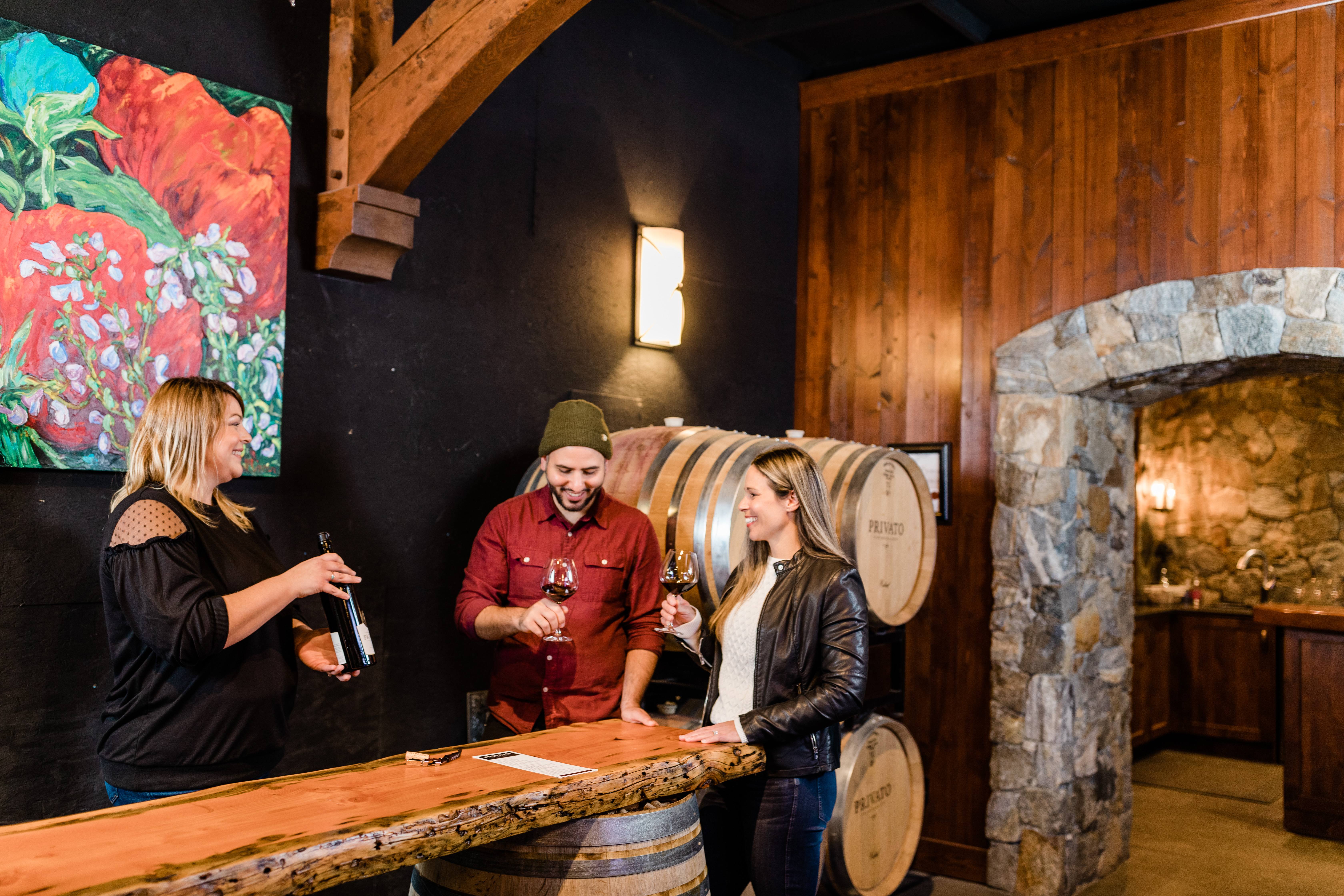 A couple tasting red wine in an indoor tasting room while a staff member talks to them