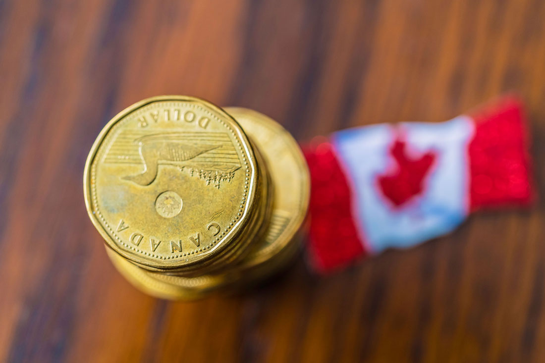 A stack of loonies with a Canadian flag behind them