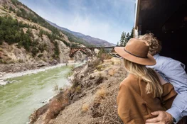Couple look out at bridge and river from Rocky Mountaineer train viewing platform
