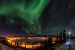 Person standing on a snowy hillside looking up at the Northern Lights in Whitehorse 