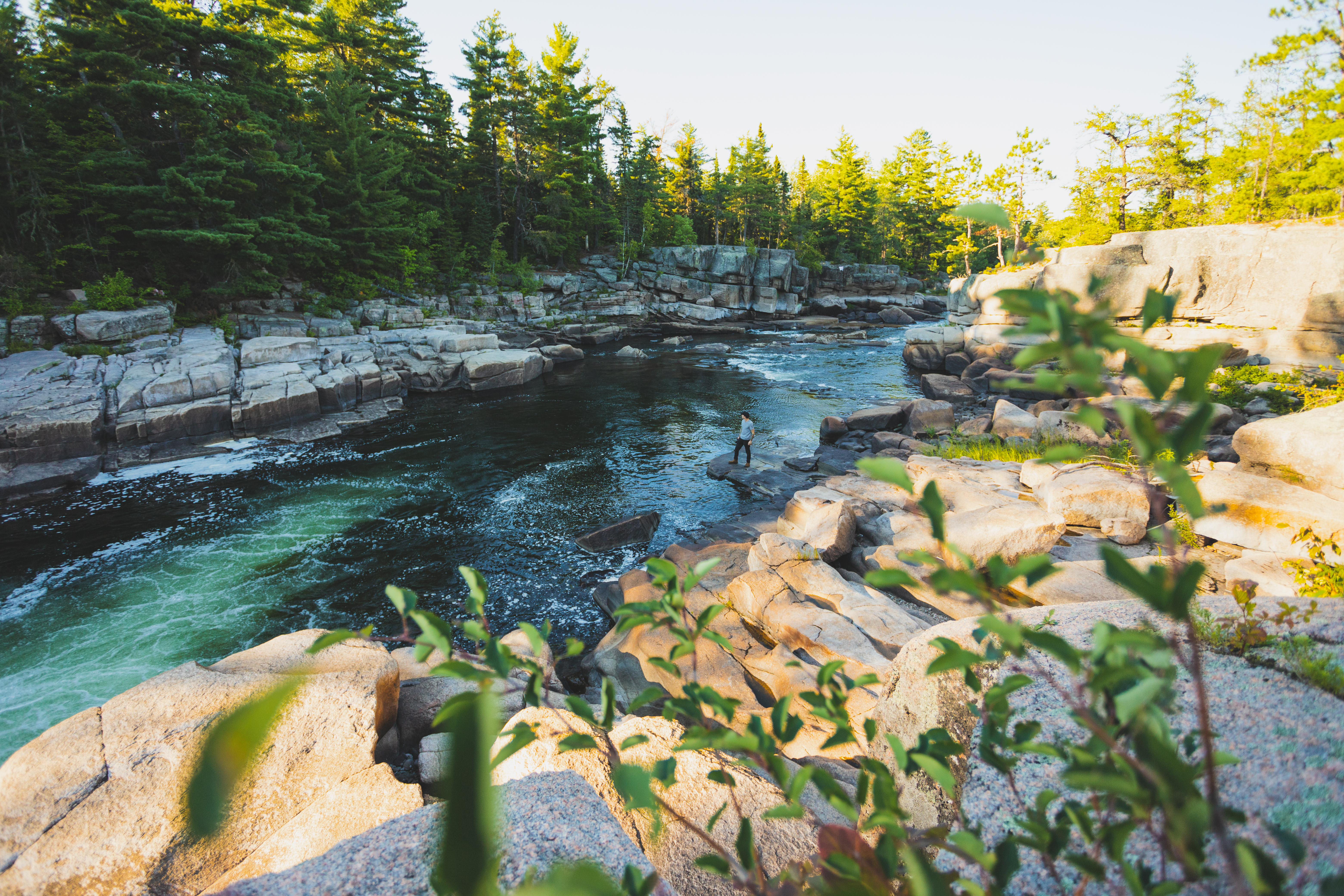 Man stands by crystal clear and coursing turquoise river waters of Pabineau Falls, in the Chaleur Region, near Bathurst