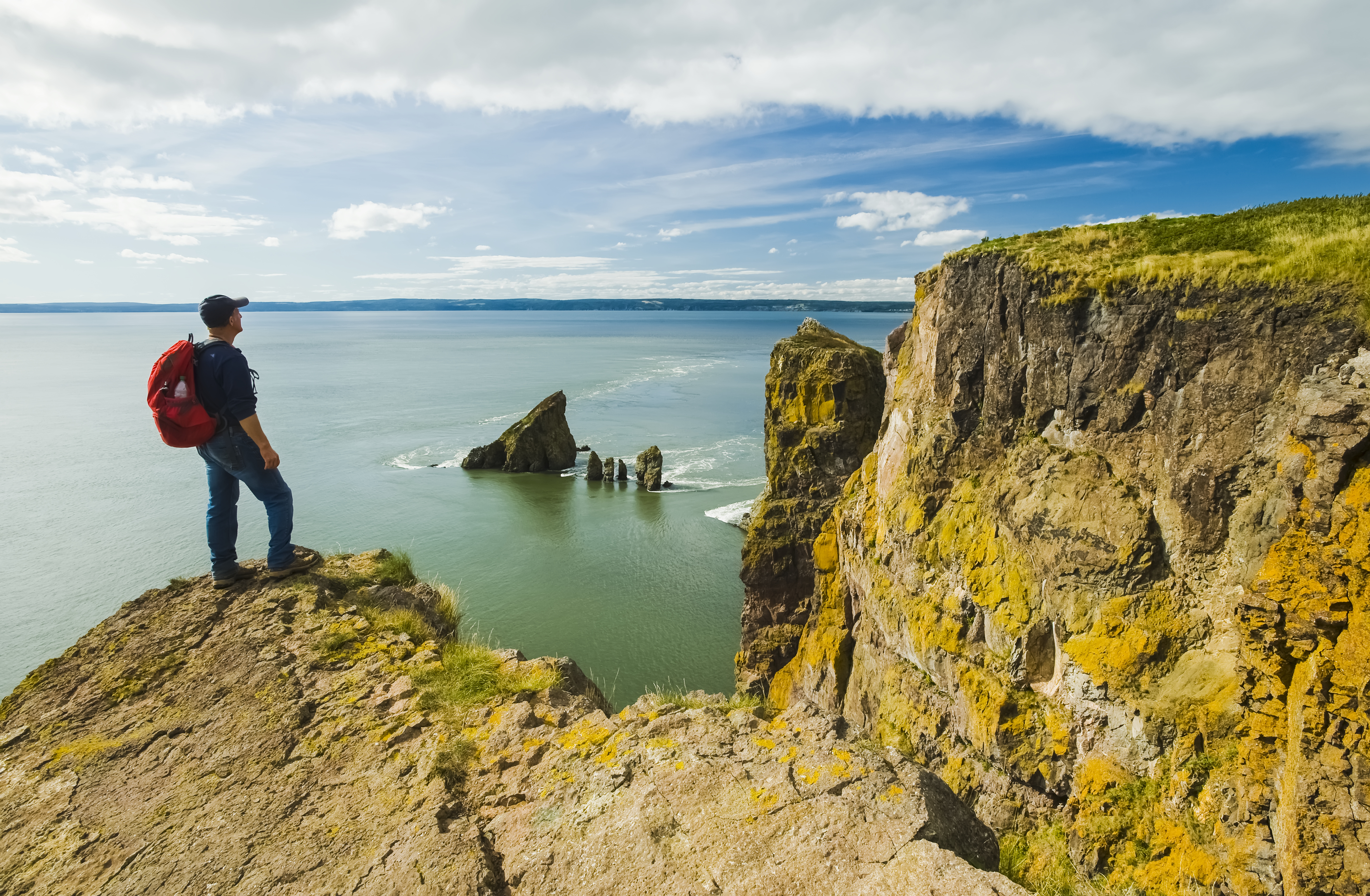 A hiker stands on a cliff edge looking over the Bay of Fundy in Nova Scotia