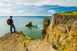 Elderly man with a backpack on reaches coast and stands on yellow coloured cliff in Nova Scotia's Cape Split