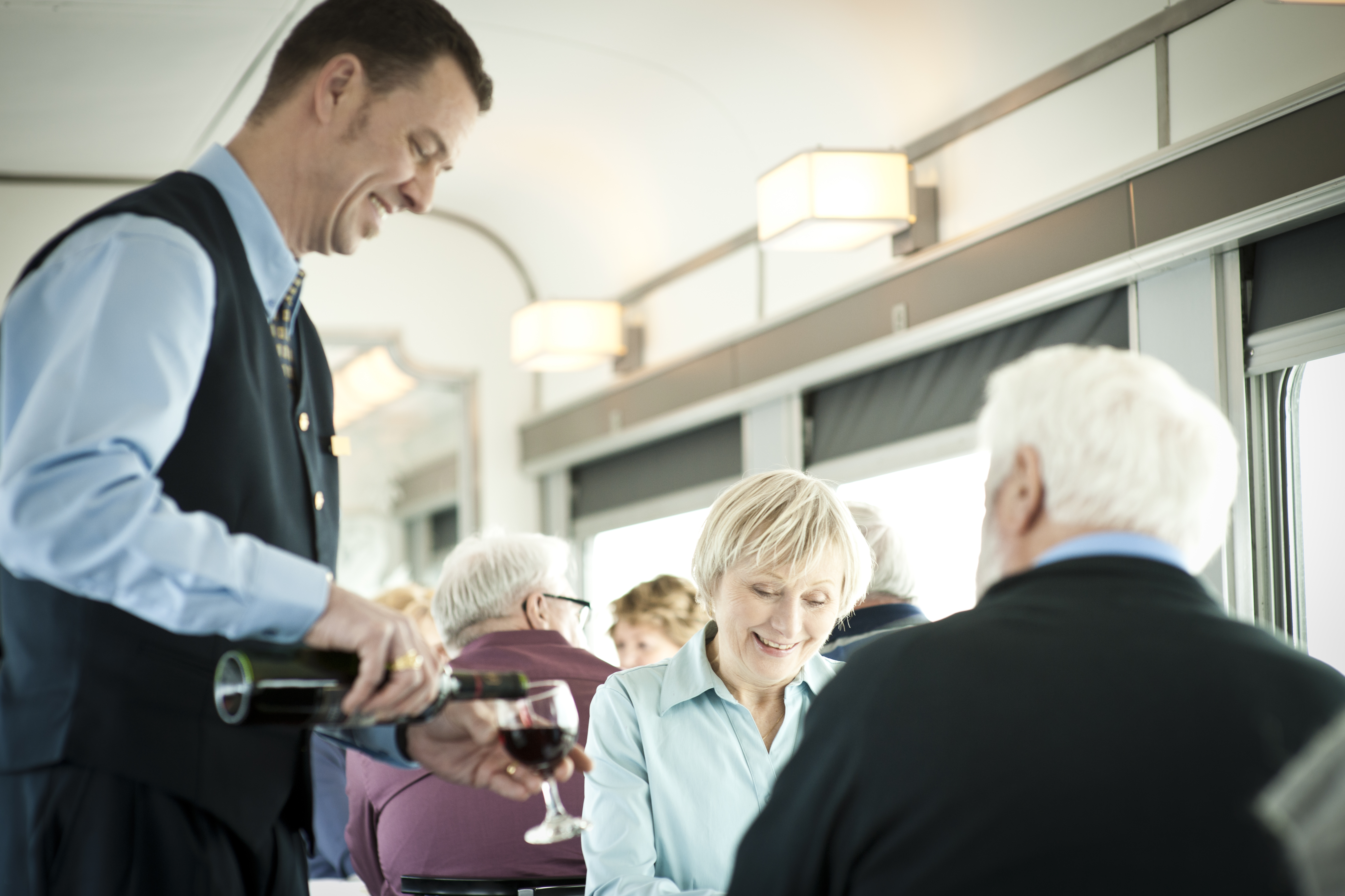 A VIA Rail train host serves wine to a senior couple in the dining car