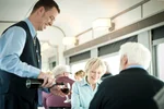 A VIA Rail train host serves wine to a senior couple in the dining car