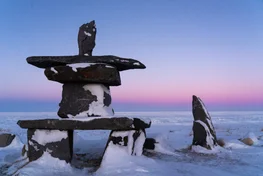 Inukshuk rock statue on the snowy tundra at sunset