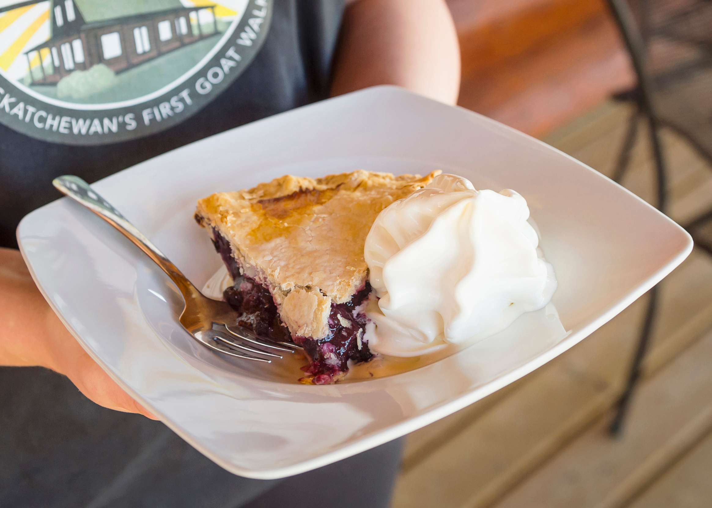 A close-up shot of a slice of Saskatoon Pie plated with a scoop of ice cream on its side