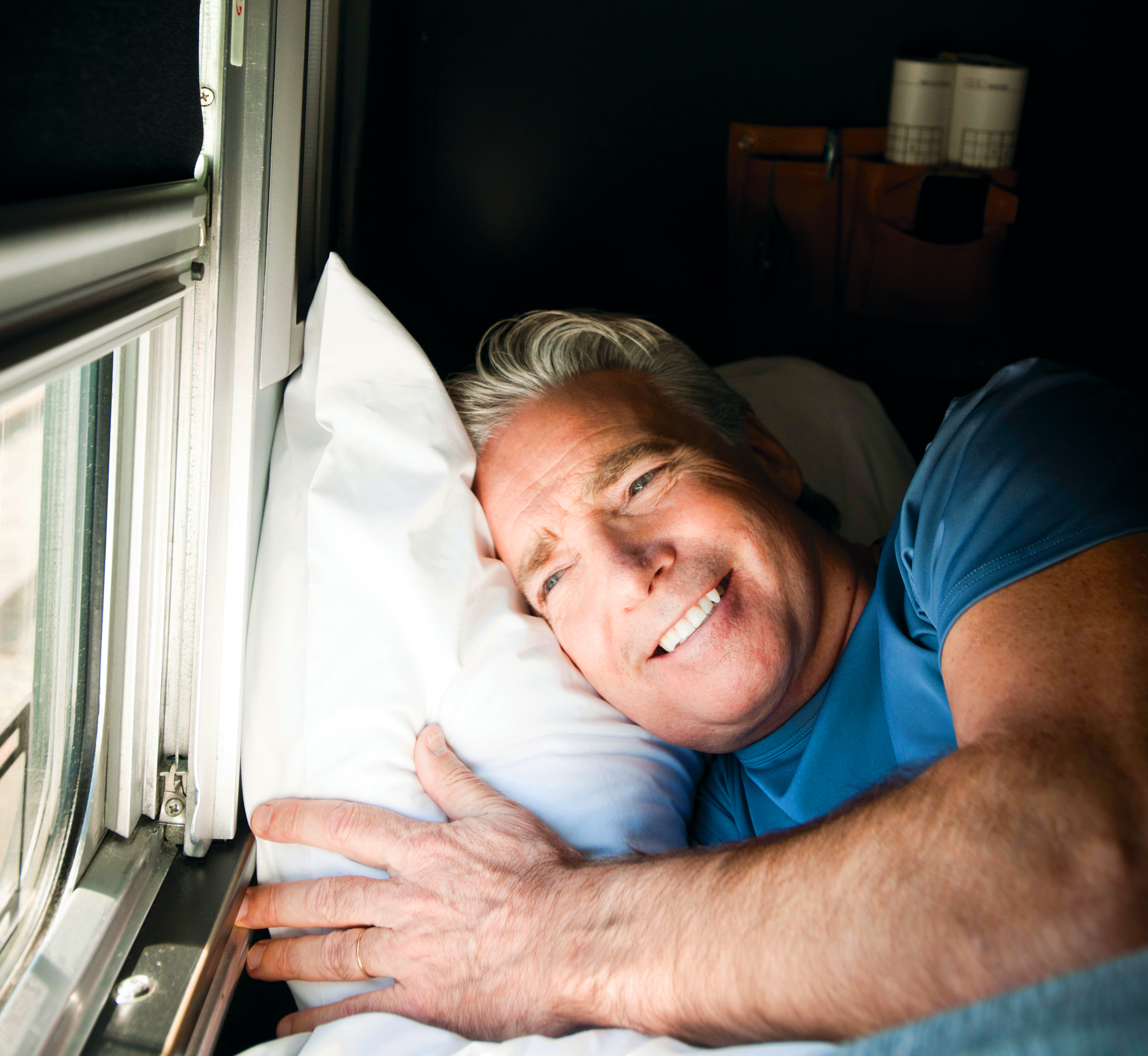Man laying in bed in sleeper cabin looks out of window