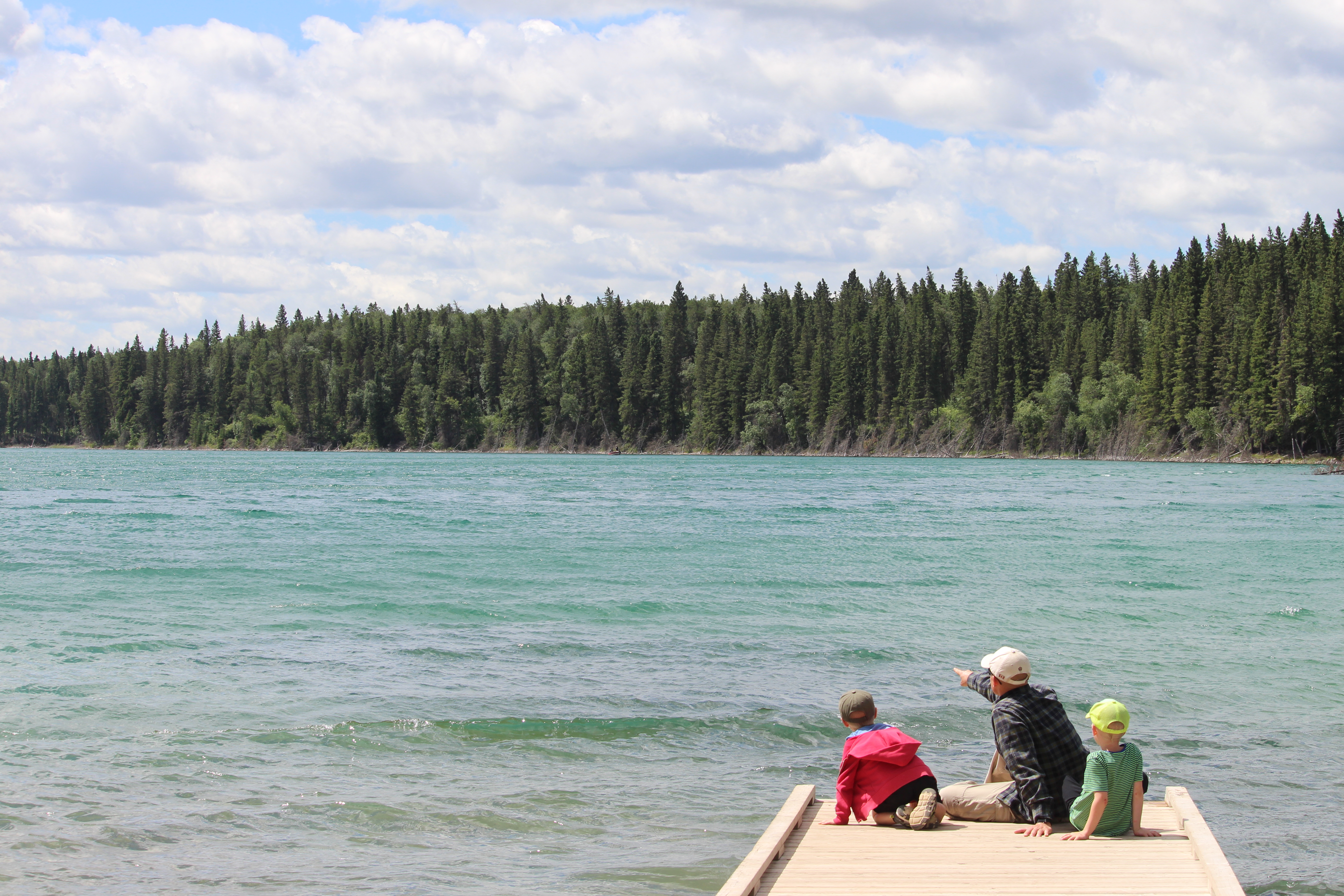 A man and two children sit on a dock and look out at East Blue Lake and the surrounding forest