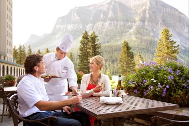 Couple sitting on.a terrace being served by a chef