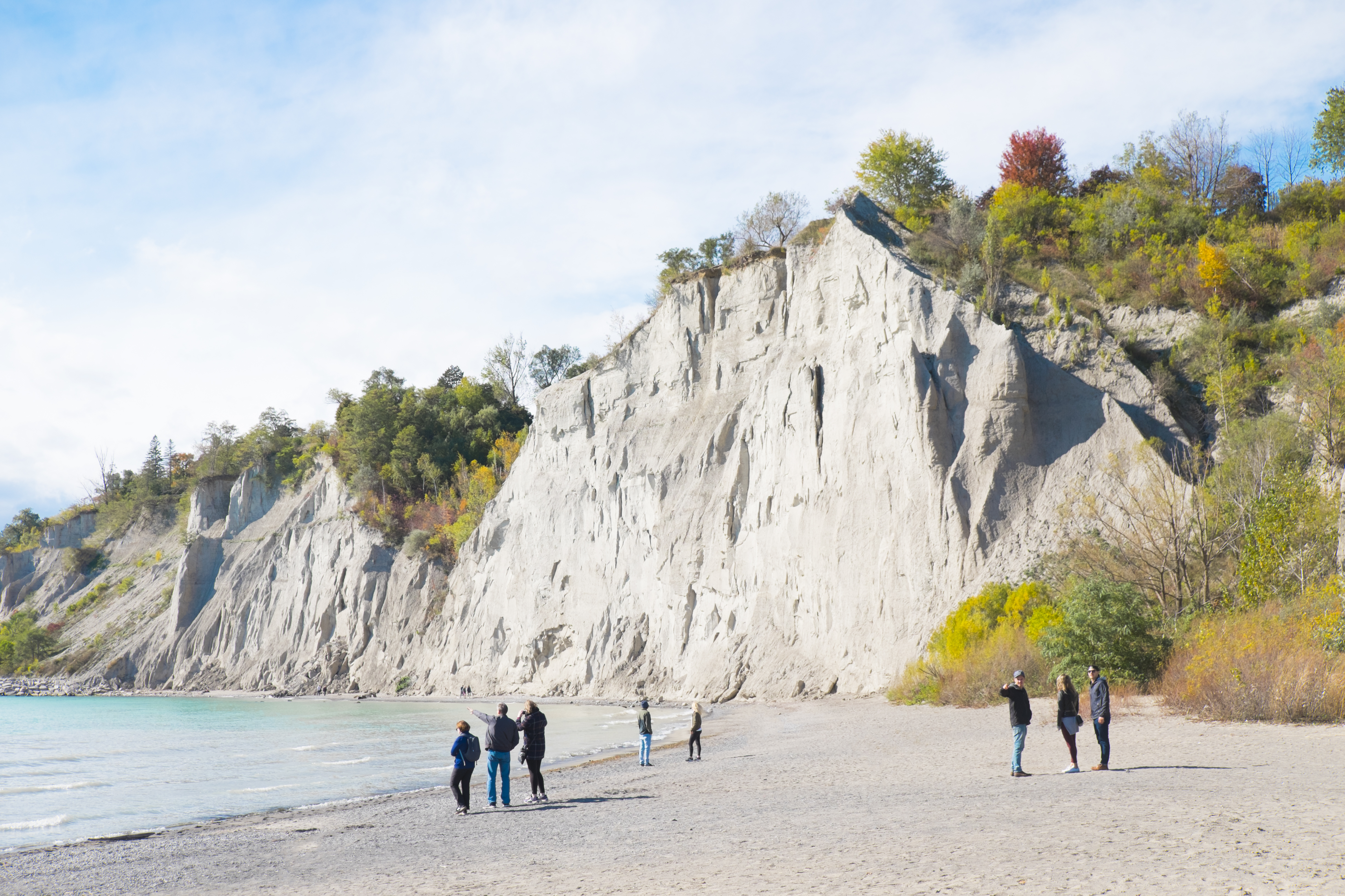 People visiting beach by bluffs with colourful trees