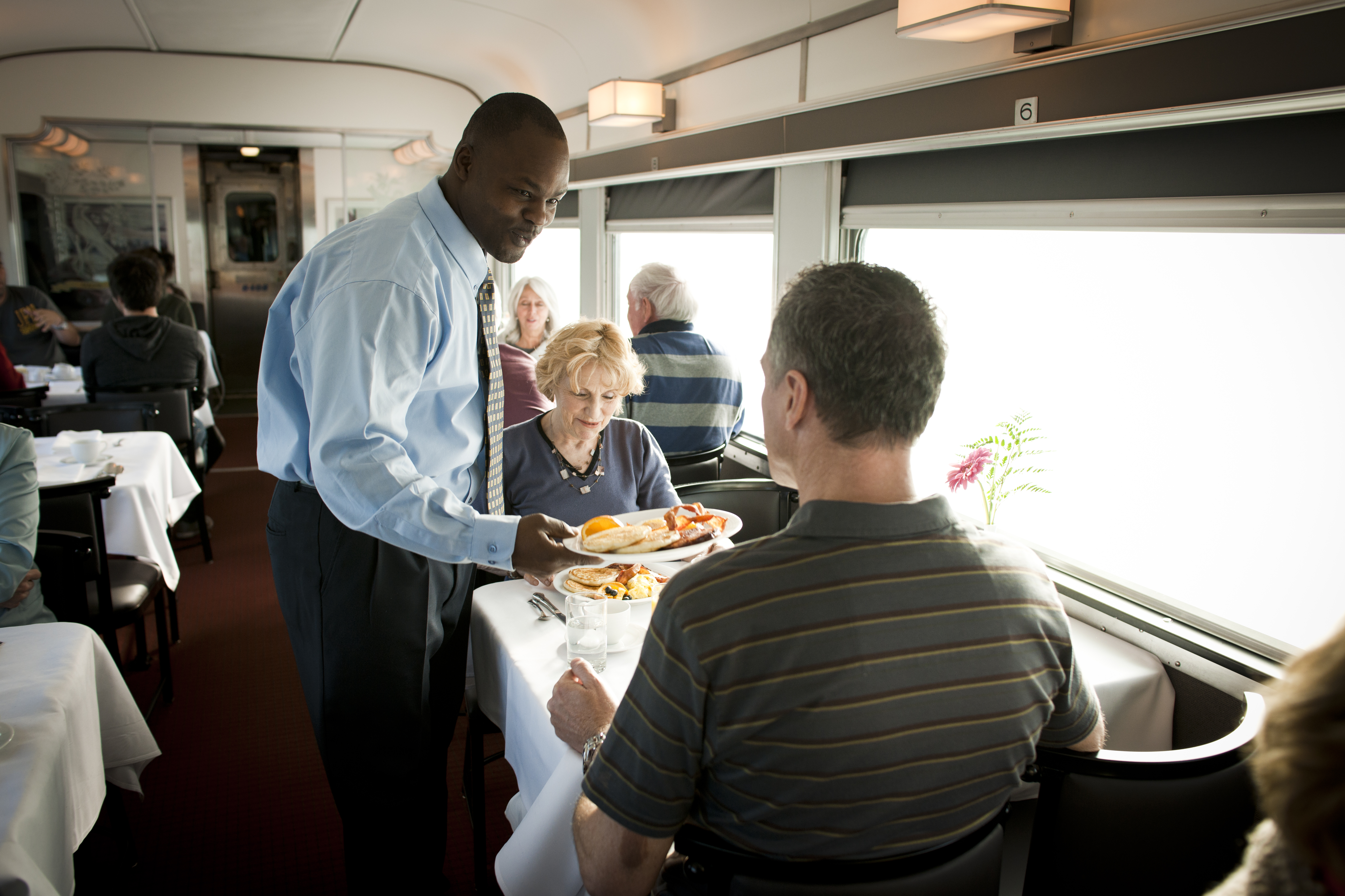 A VIA Rail attendant serves food to a senior couple in the Sleeper Plus dining car