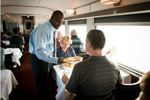 A VIA Rail attendant serves food to a senior couple in the Sleeper Plus dining car