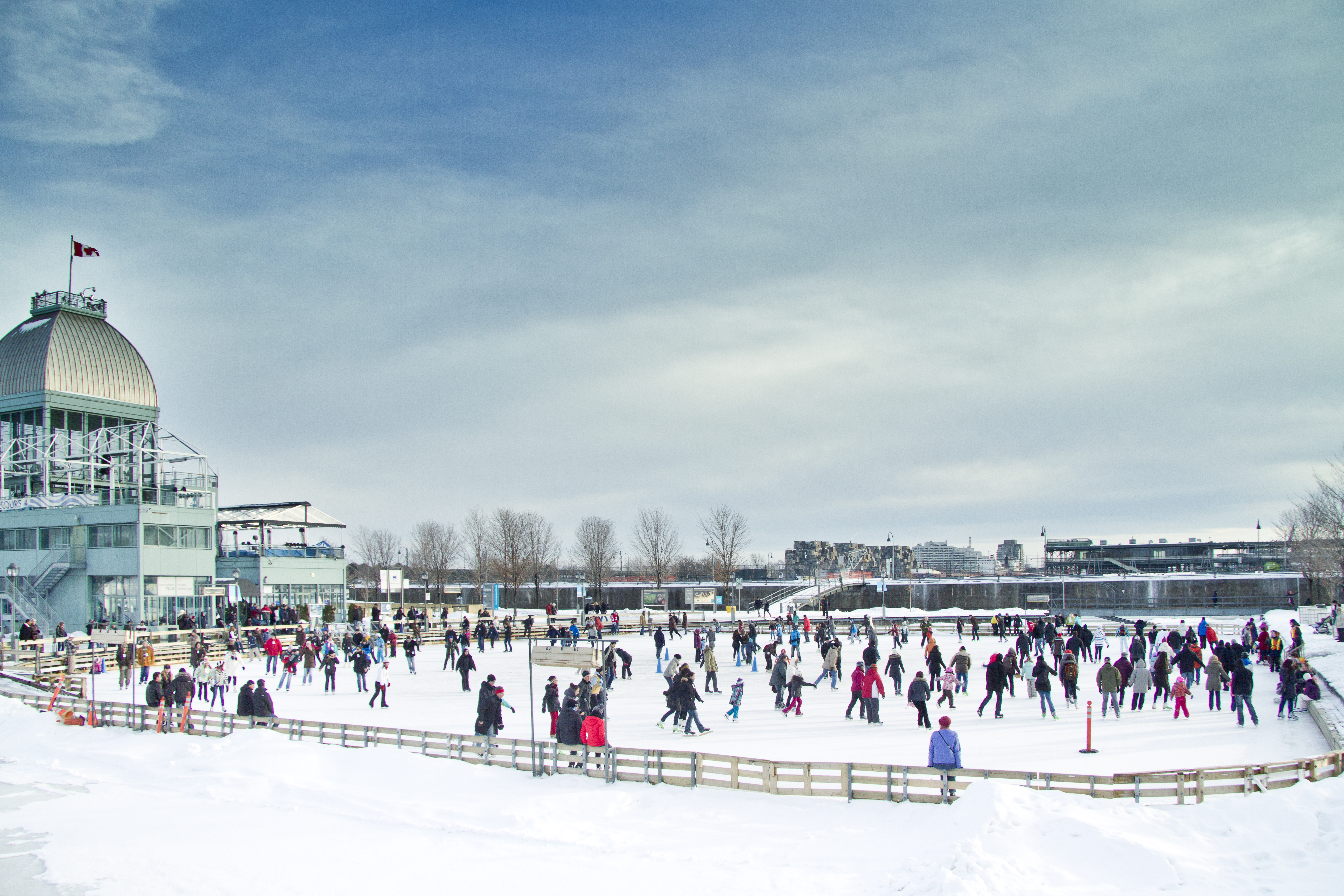 Busy outdoor ice skating rink in Old port of Montreal, cloudy skies above