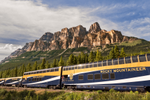 A Rocky Mountaineer train with glass-dome coaches travels past Castle Mountain in the Rockies