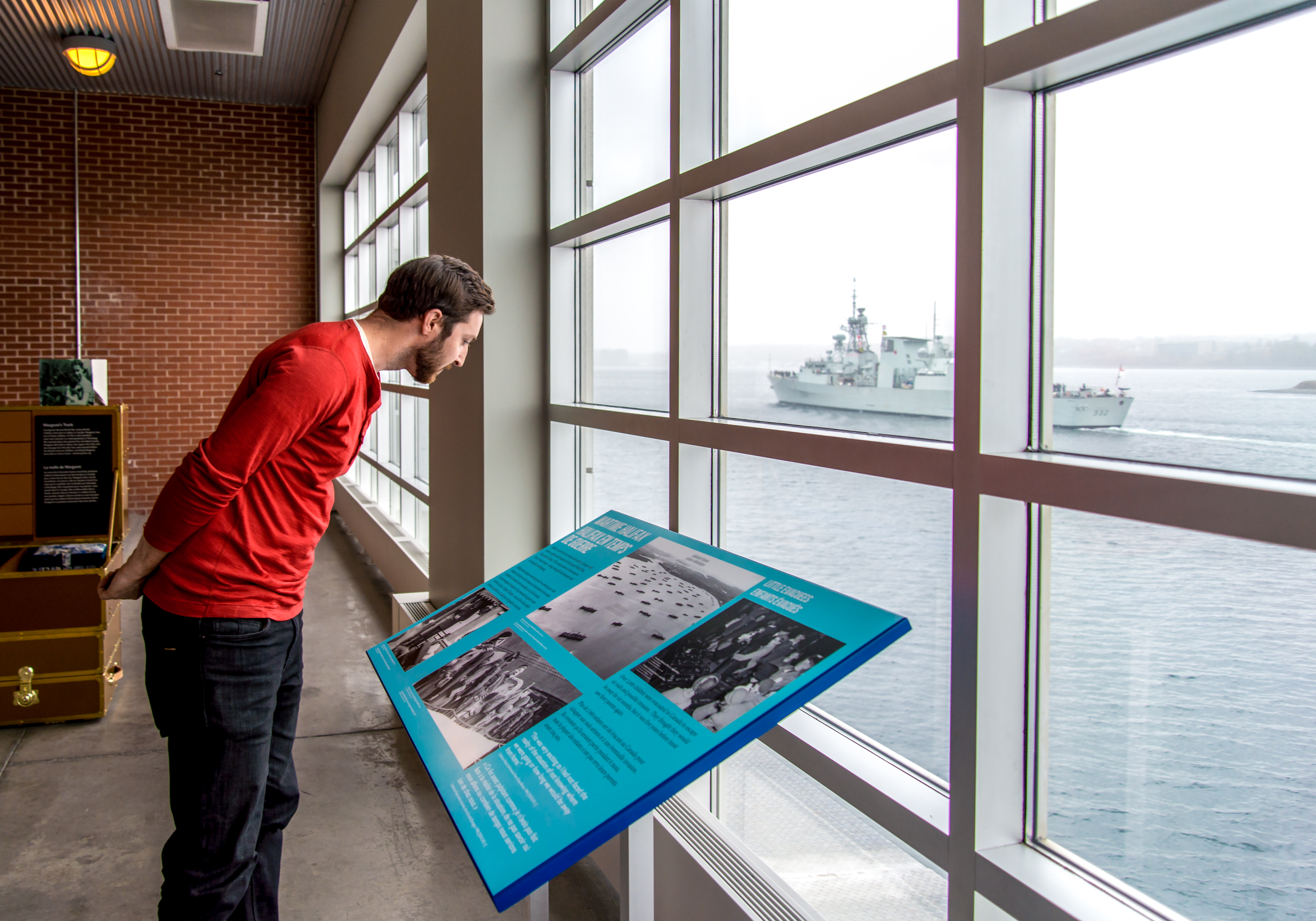 Peron reading an information board next to large windows that look out to the ocean