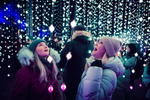 Two women in winter coats looking up at strings of lights at the Toronto Light Festival