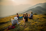 A group of hikers rest and take in the view of neighbouring mountains from grassy hill