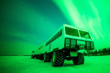 A Tundra Buggy surrounded by the display of aurora borealis