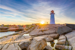 A person standing next to a lighthouse on a rocky shoreline as the sun sets