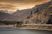 VIA Rail's Canadian Train traveling around the rocky mountains with water in the foreground.