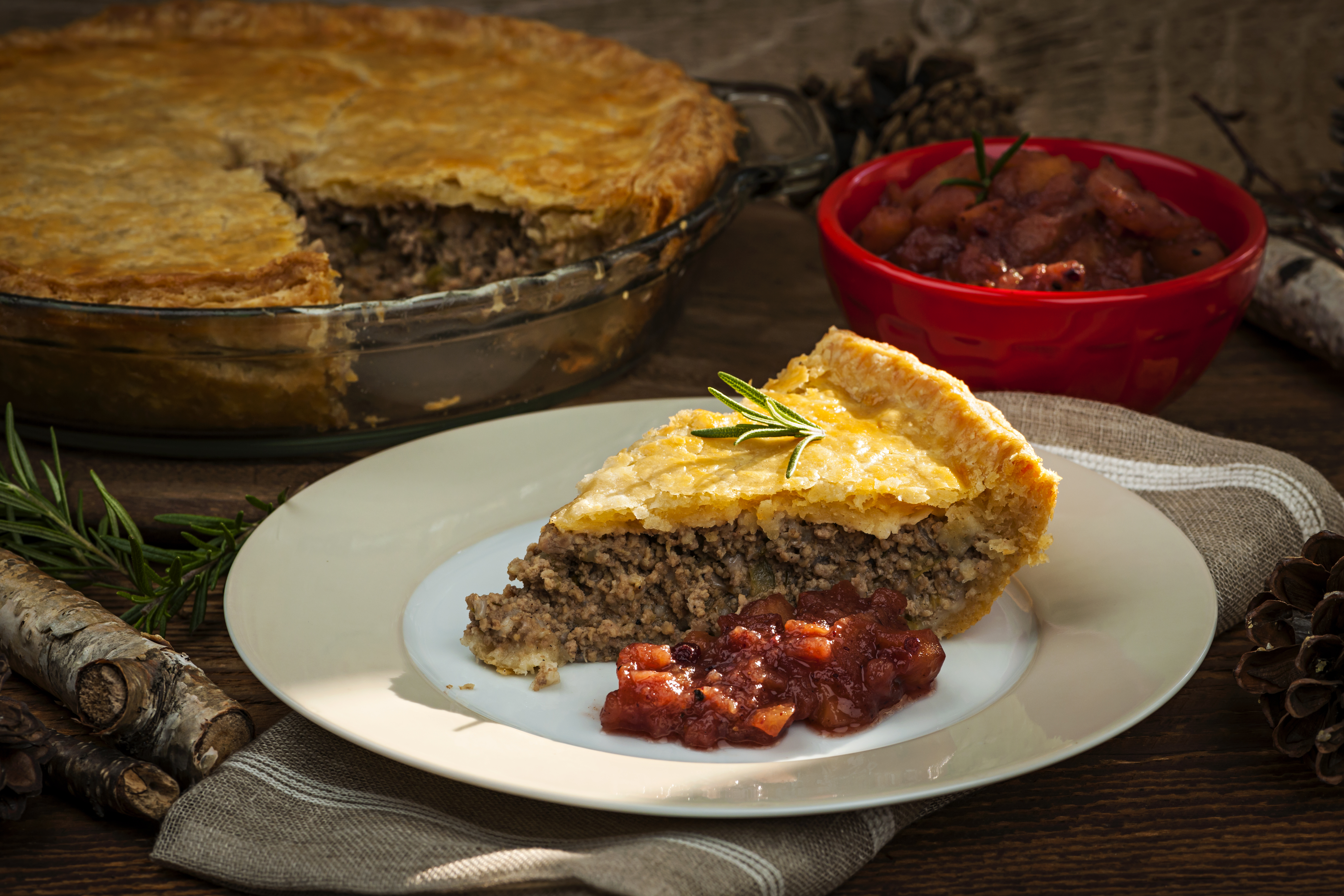 Slide of a Quebec meat pie (tourtiere) on a plate and small bowl of chutney 