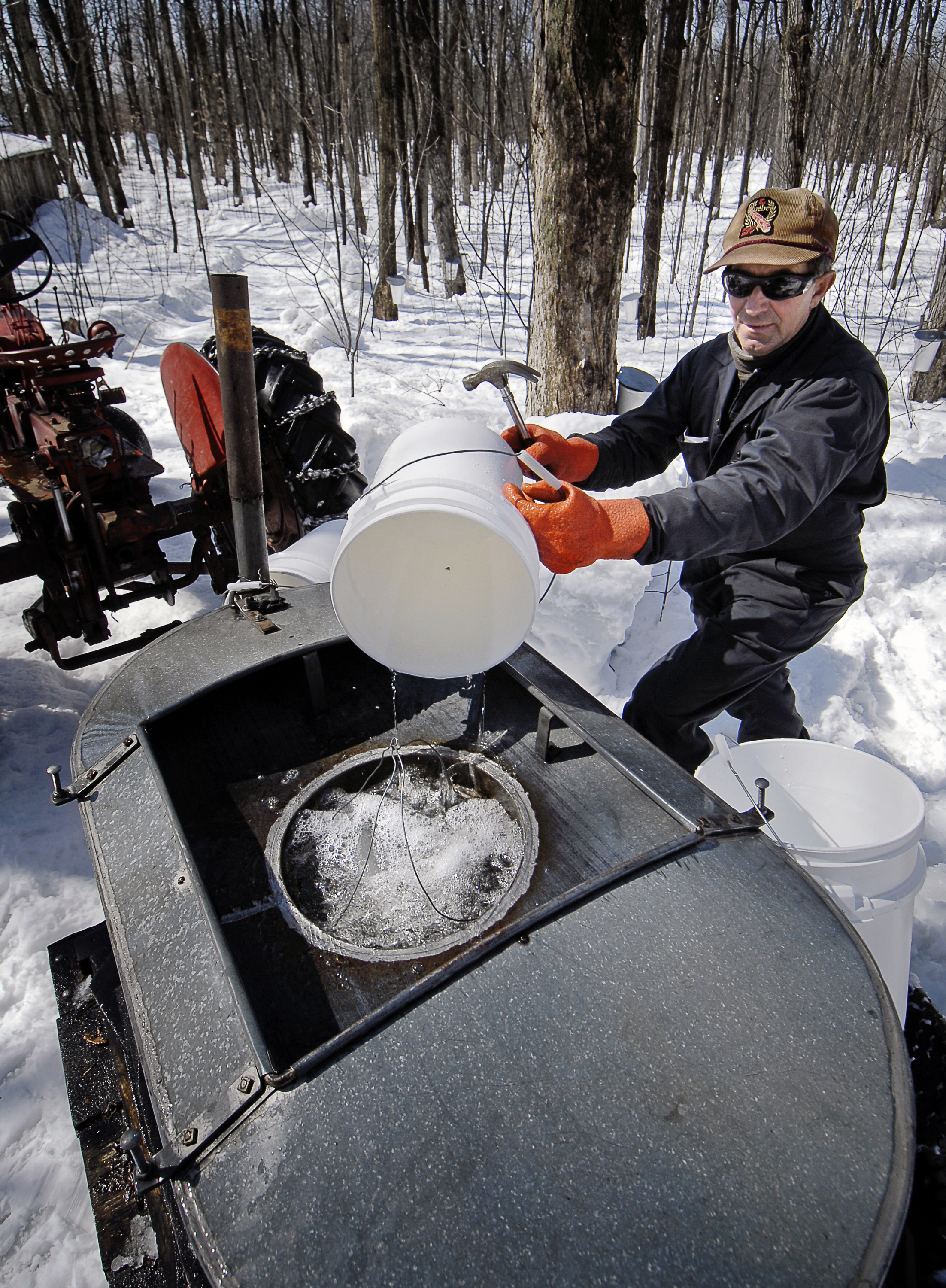 A man working outdoors on the production of maple syrup, snow on the ground and bare trees