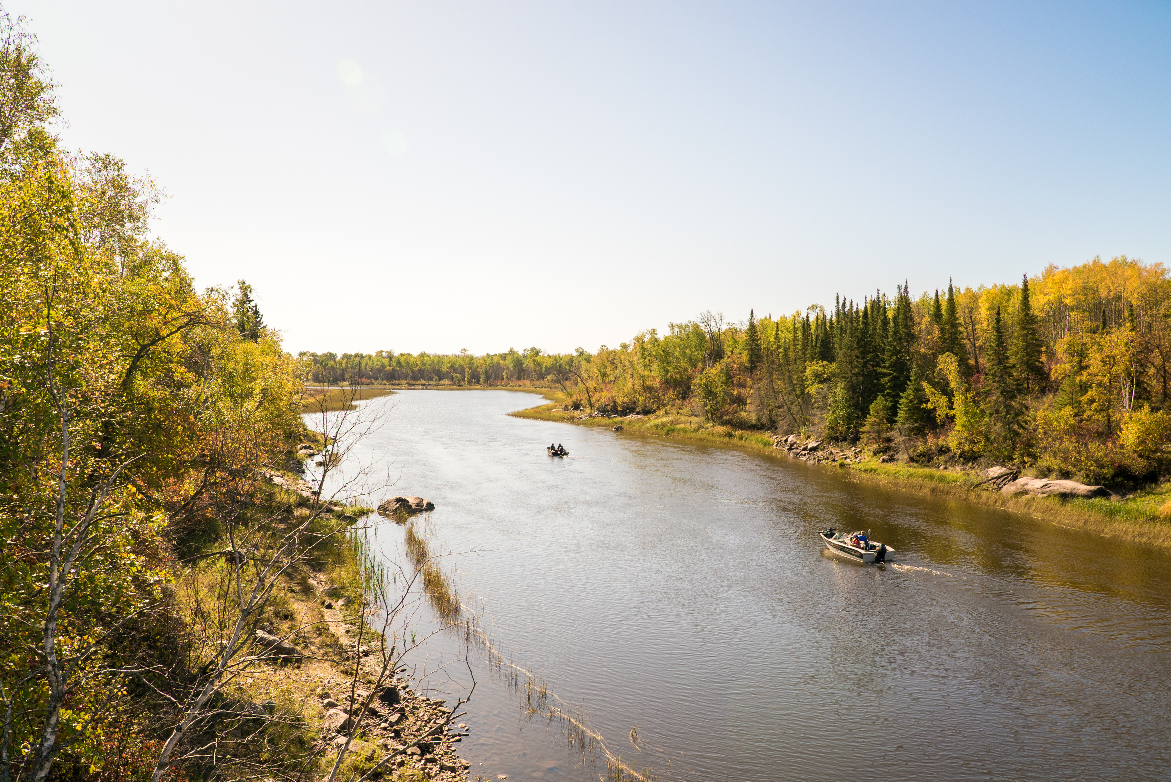 Boats cruising on Nutimik Lake, fall colours on each side