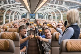 Rocky Mountaineer onboard Host gives welcome toast in GoldLeaf dome as guests cheers.