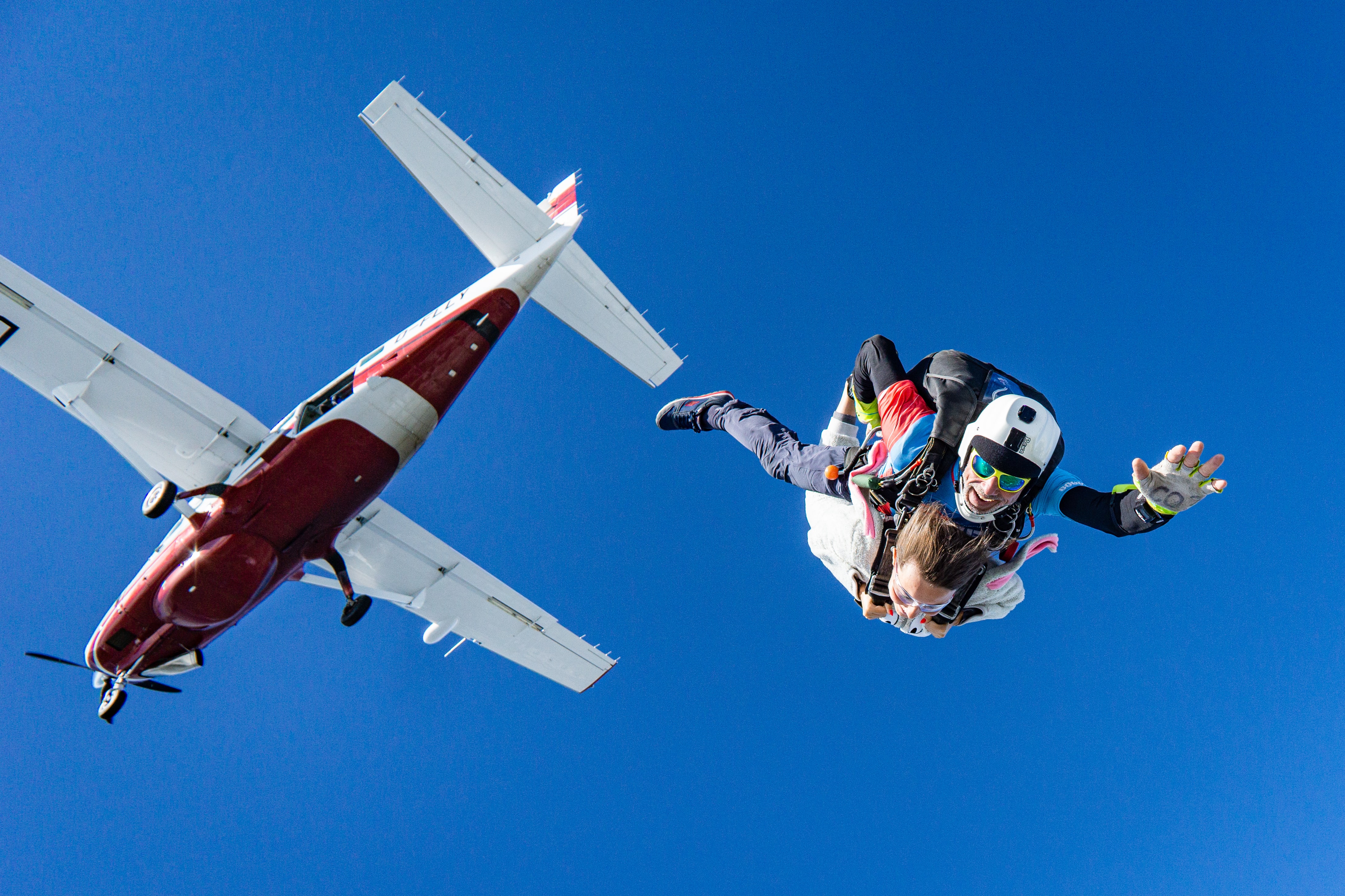 Tandem skydivers have just jumped out of a red and white airplane