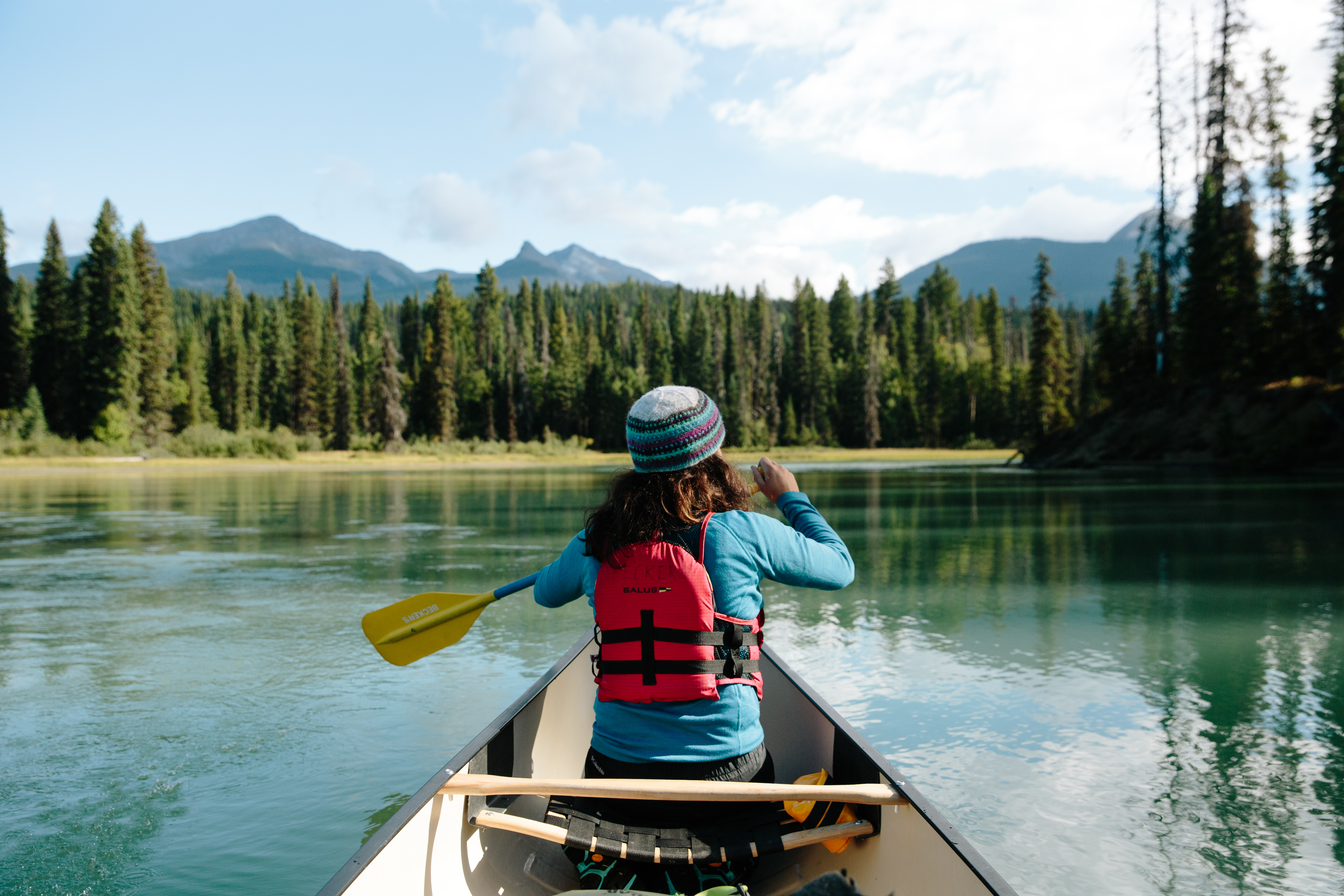 A woman sits in the front of a canoe and paddles across a lake near Quesnel 