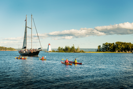 a small group of kayaks coming up to a sailboat with a lighthouse in the distance