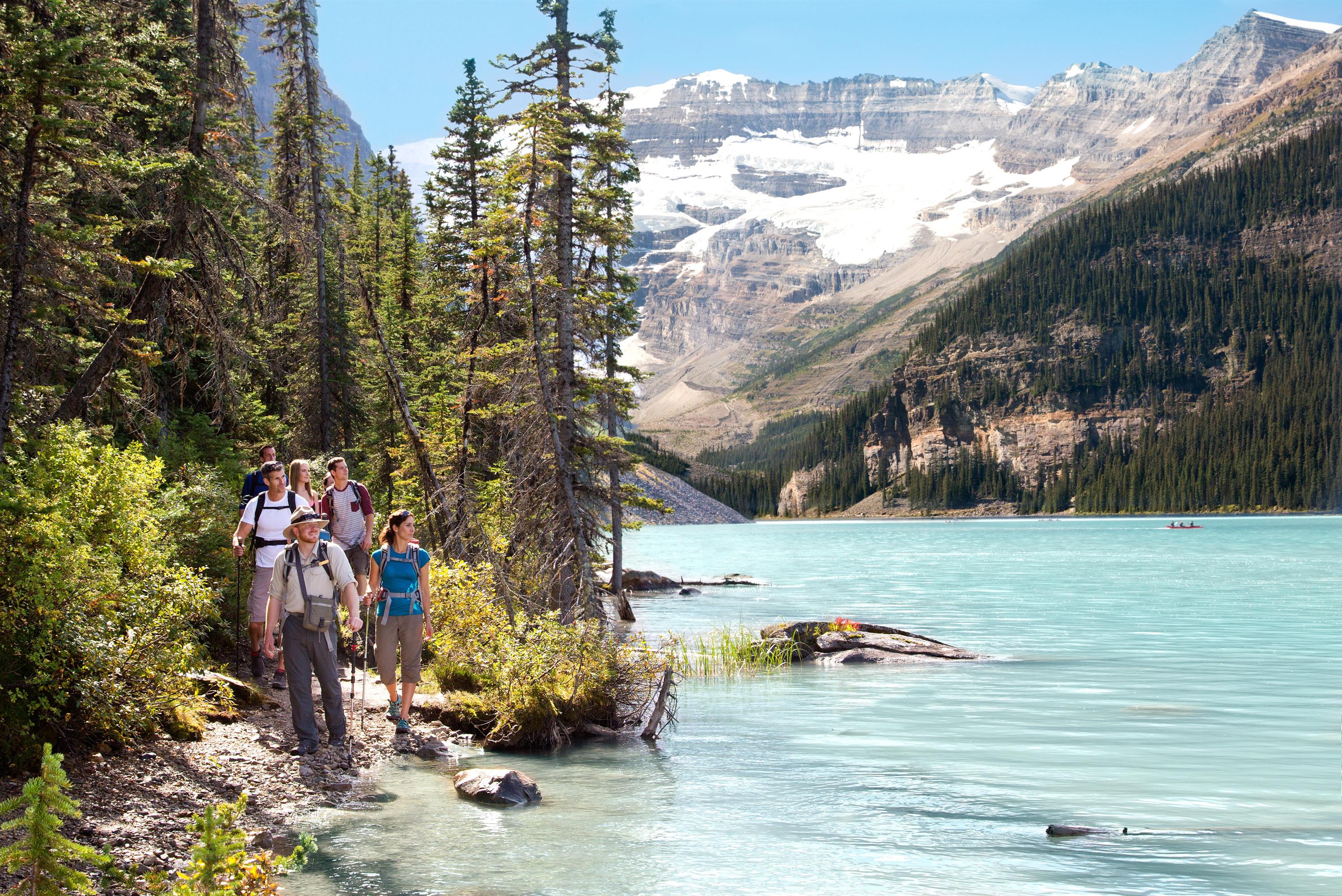 A guide leads a group of hikers along a trail beside the blue waters of Lake Louise