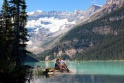 Couple sitting on the edge of the turquoise waters of Lake Louise