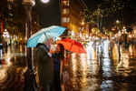 A senior couple holds umbrellas as they walk through Gastown during a rainy evening