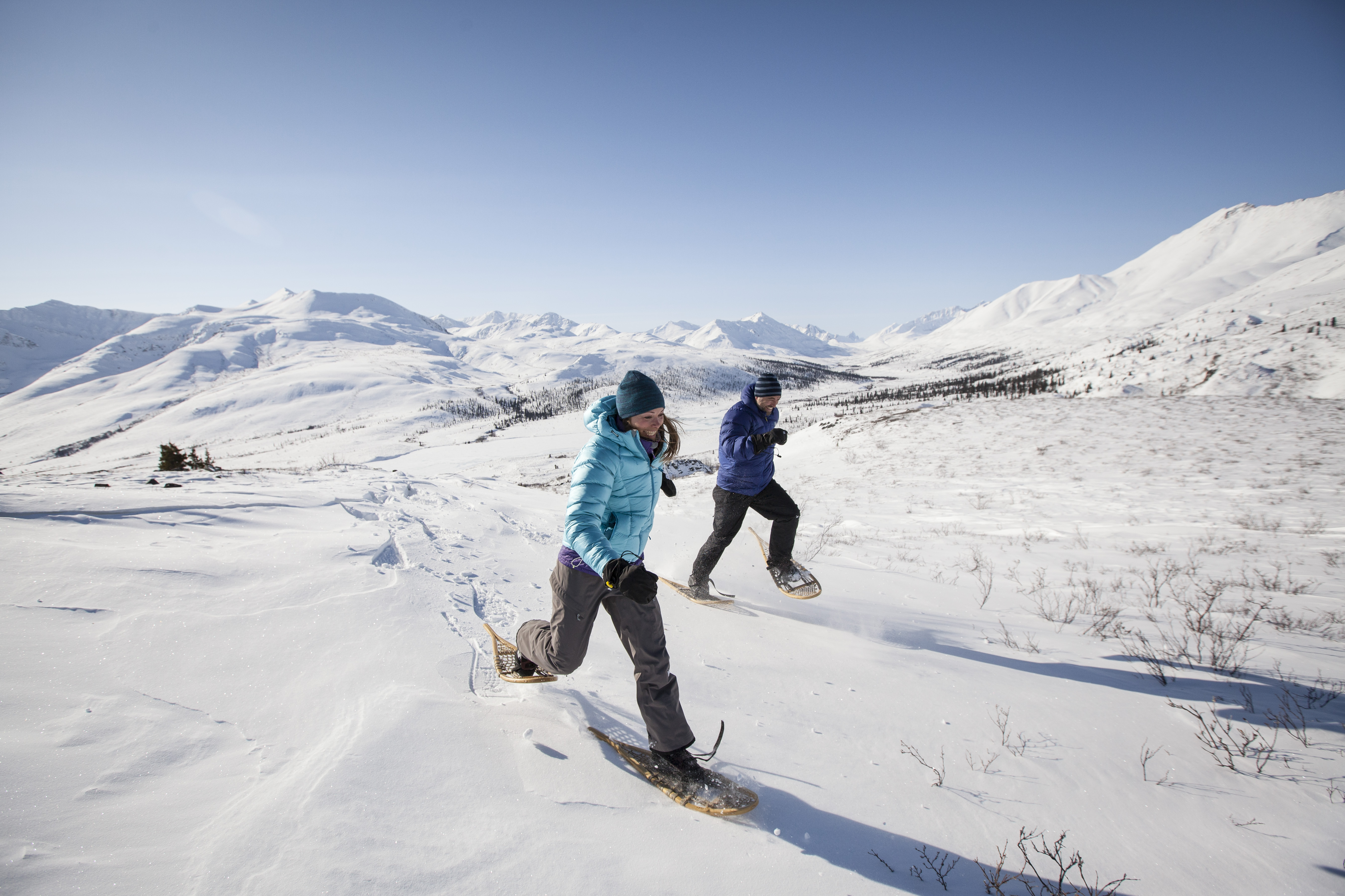 A couple snowshoeing over a snowy plain with mountains behind