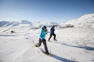 A couple snowshoeing over a snowy plain with mountains behind