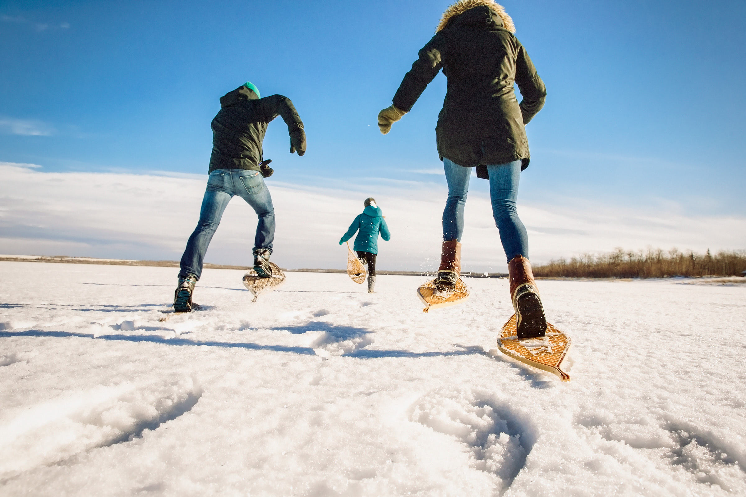 A group travelling in snowshoes leap forward leaving steps in the fresh snow on a bright and clear day