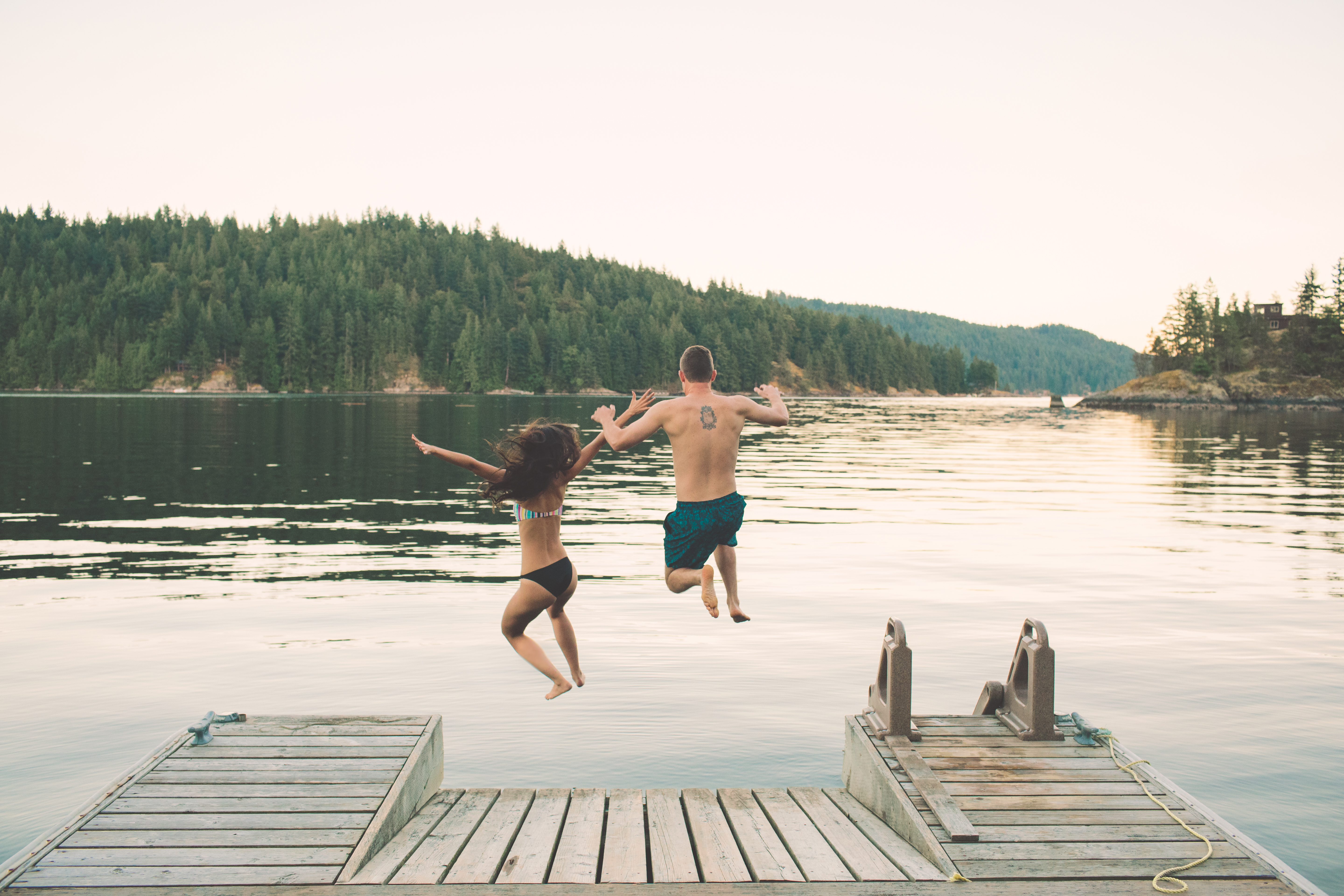 Couple jump off wooden dock into lake in Vancouver in the Summer
