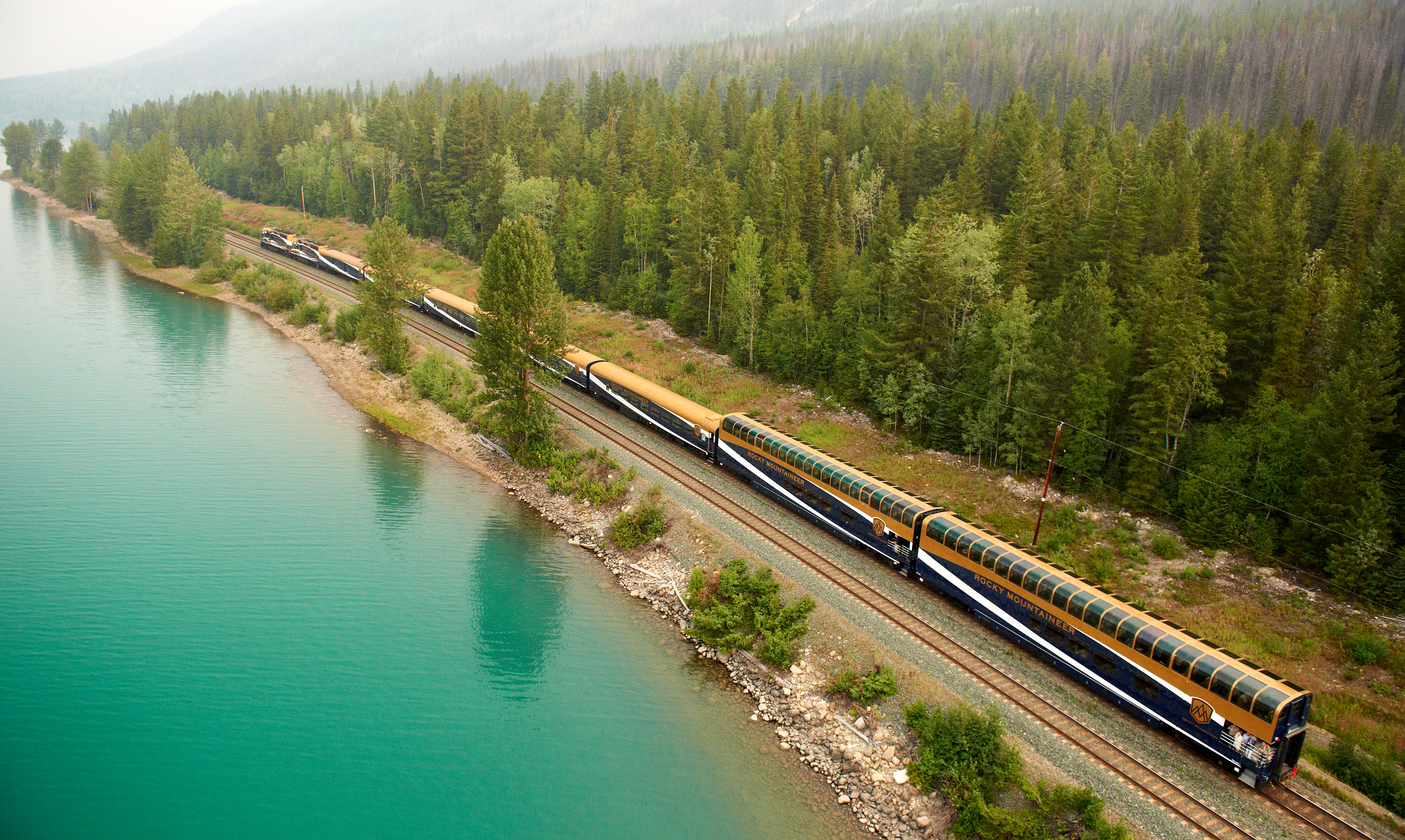 Rocky Mountaineer train travels through Banff near turquoise lake and rows upon rows of green trees