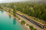 Rocky Mountaineer train travels through Banff near turquoise lake and rows upon rows of green trees