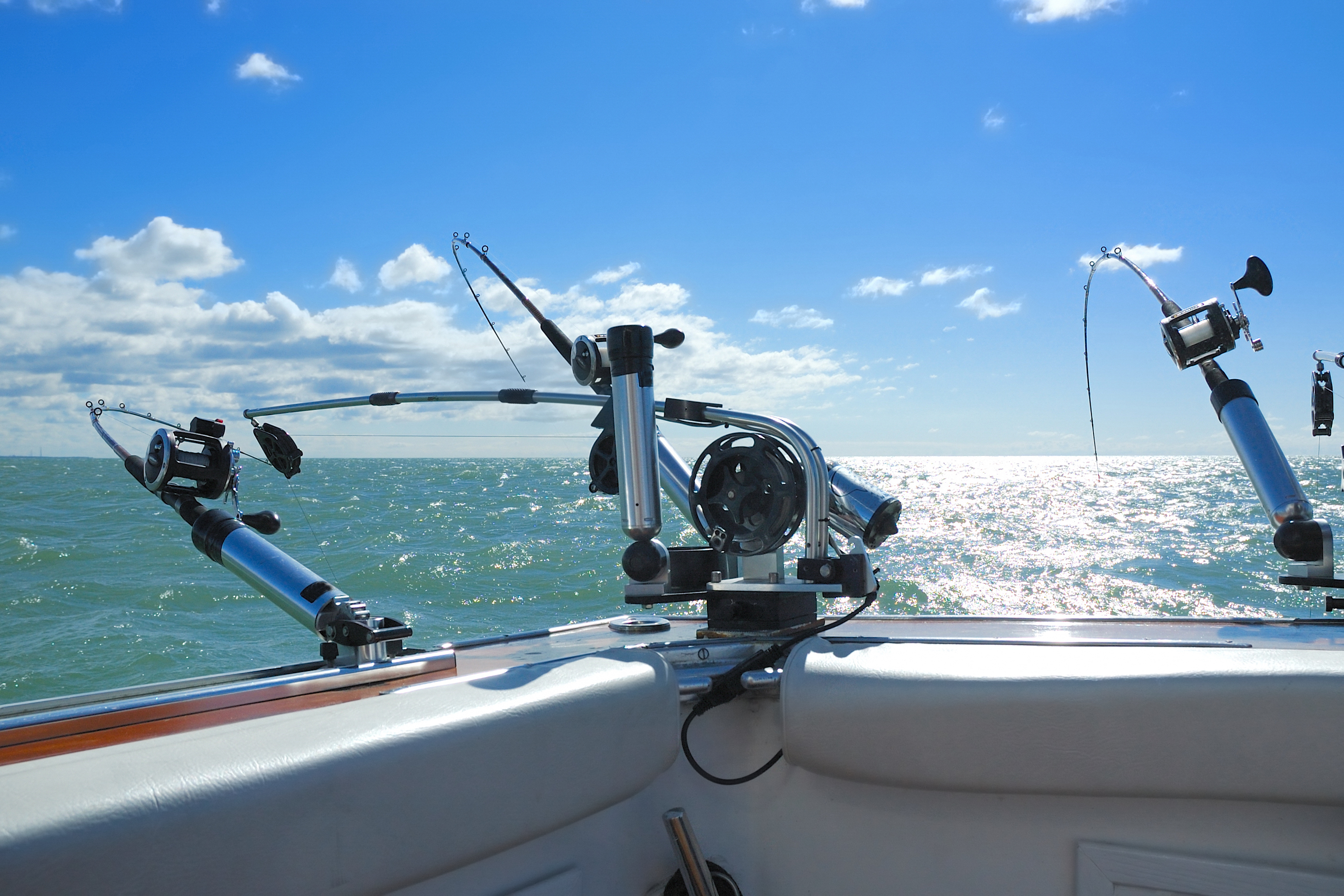 Close-up view of rod and gear for recreational fishing on board boat travelling through glistening lake
