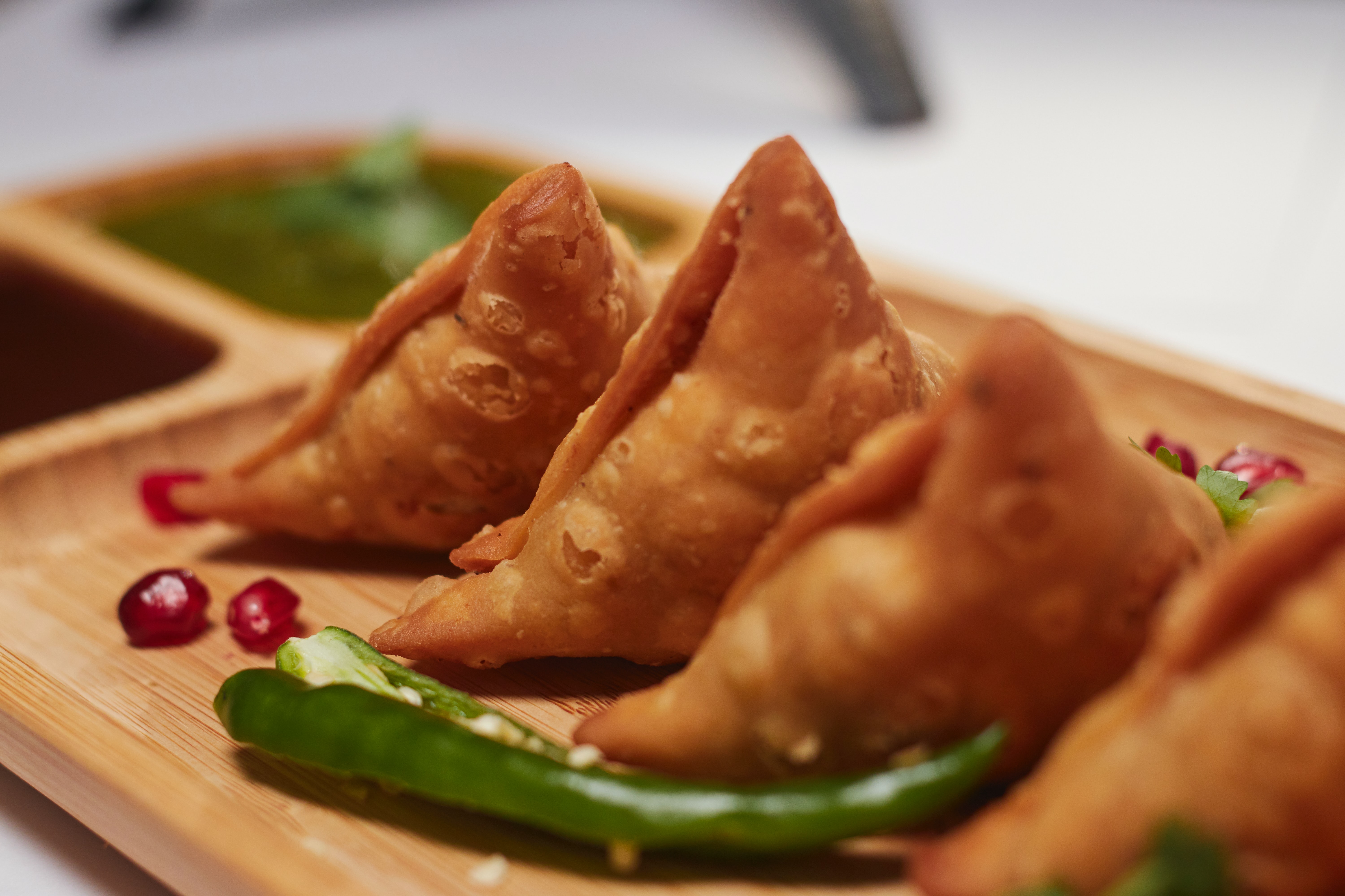 Close up of a plate of samosas and a green chilli