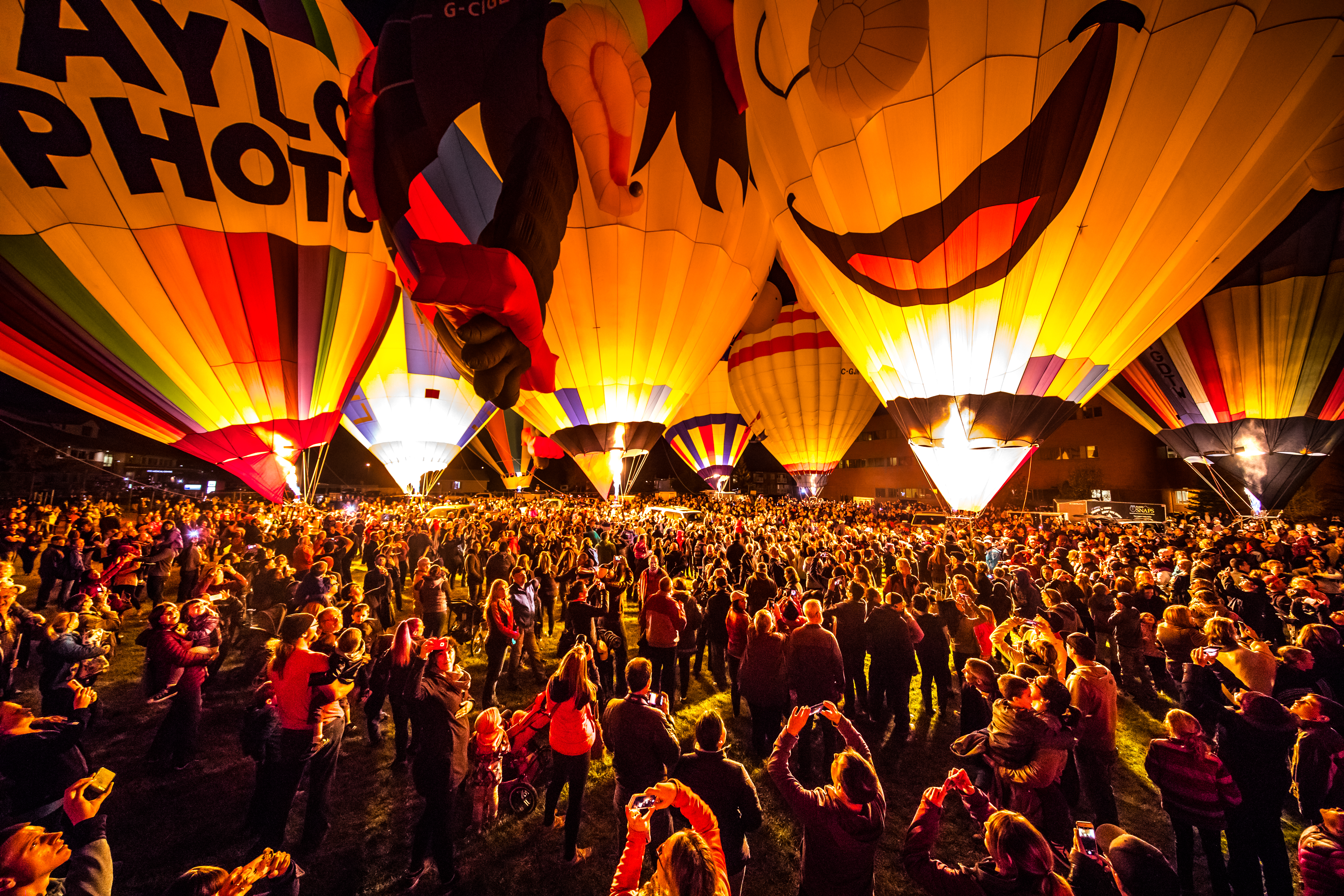 Crowd below a row of hot air balloons at night