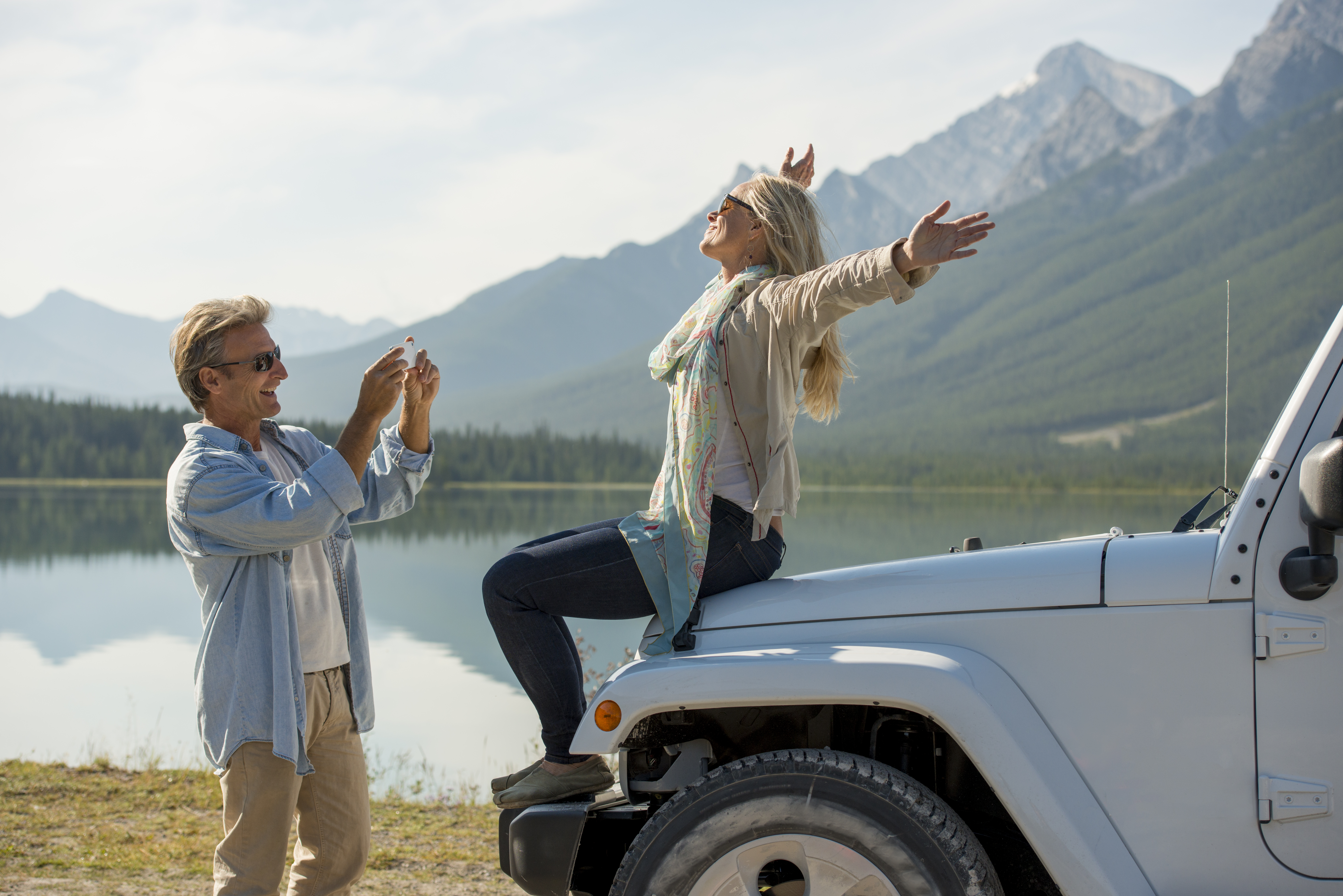 man takes picture of woman on Jeep hood, mountain lake, Alberta