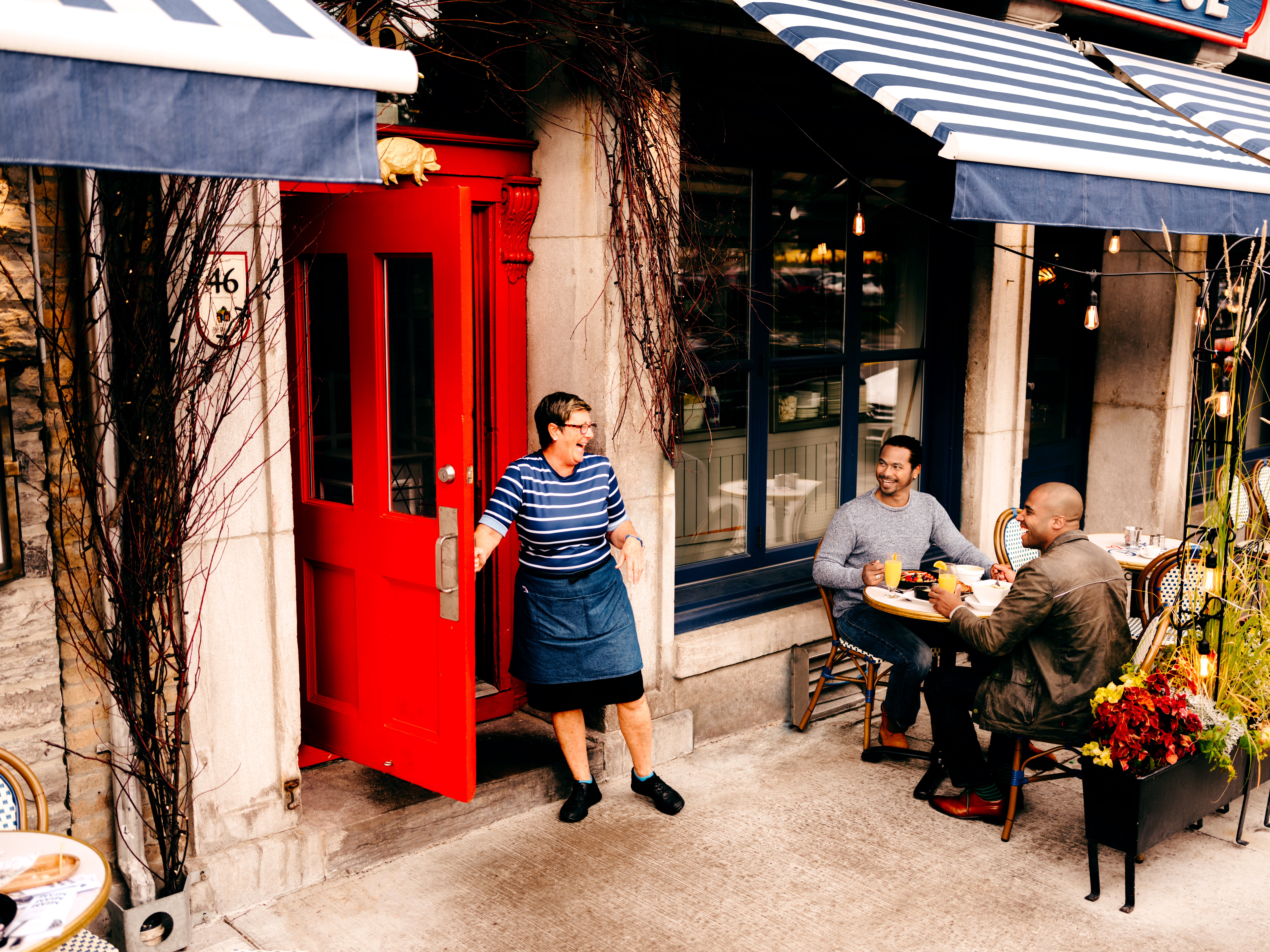 A waitress laughing with two people sitting outdoors at a restaurant