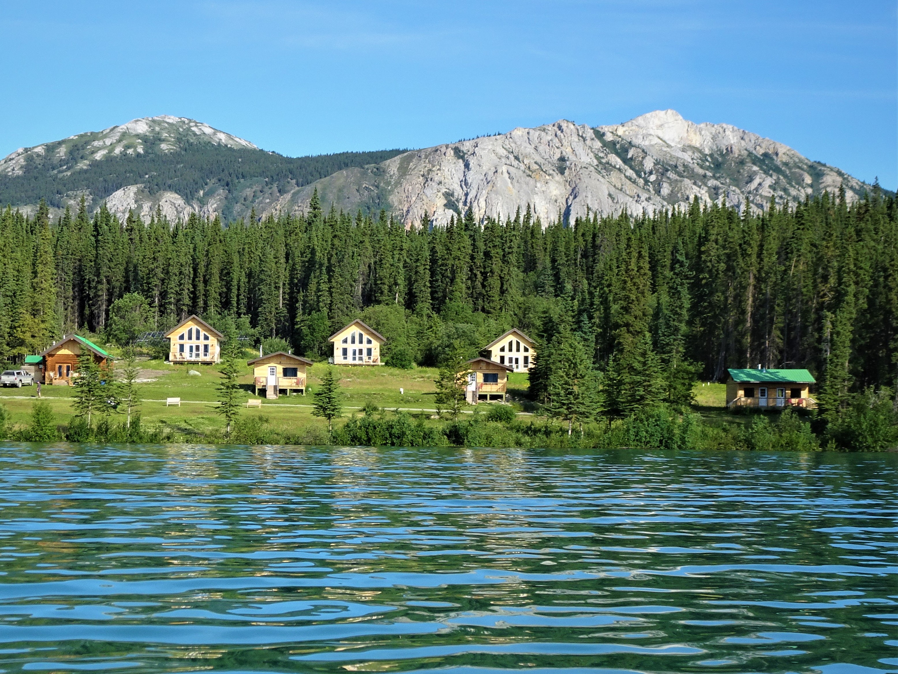 View of a blue lake in front of cabins at Southern Lakes Resort, with forest and mountains behind