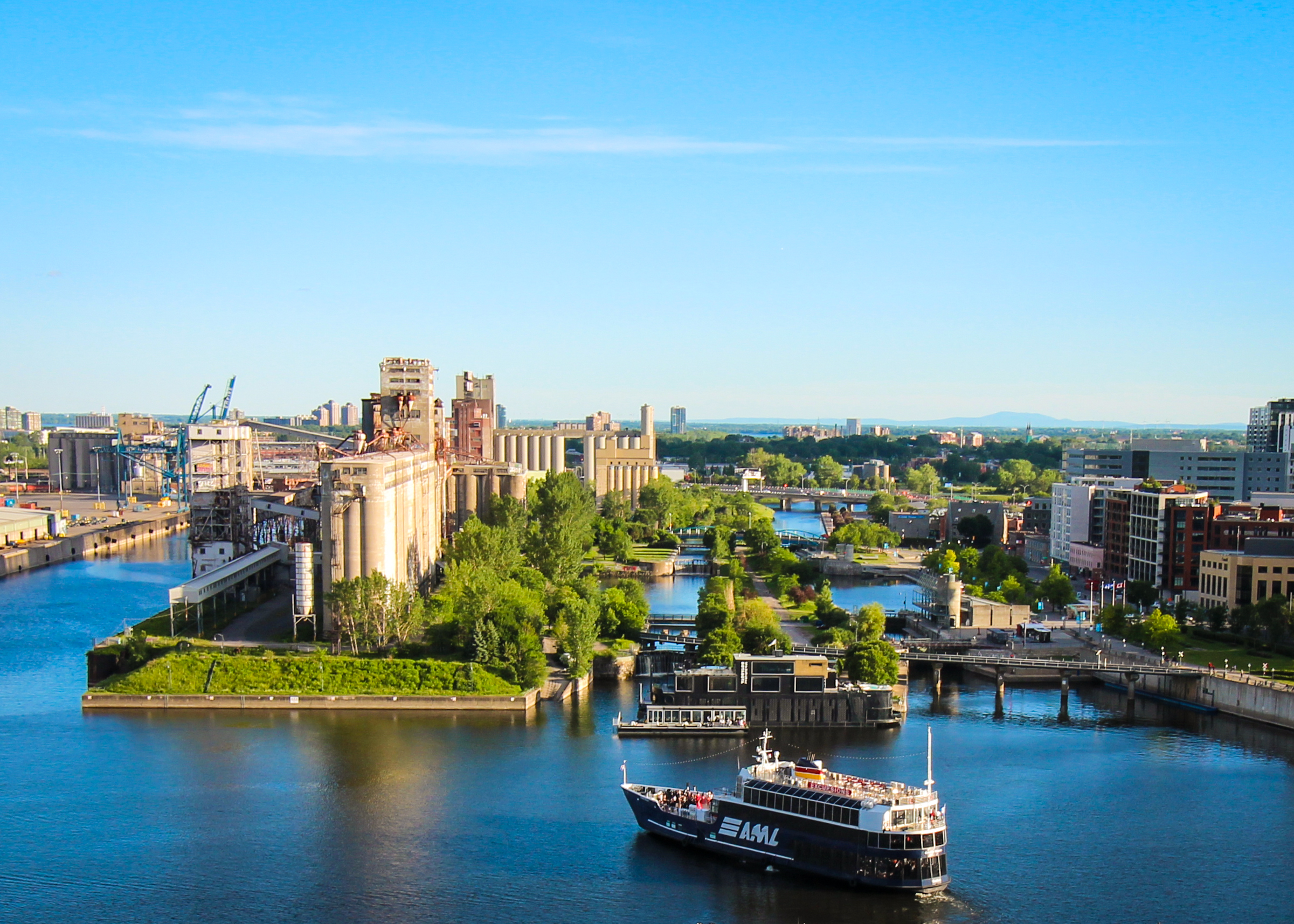 A sightseeing boat cruises along the water in Montreal's Old Port on a sunny day