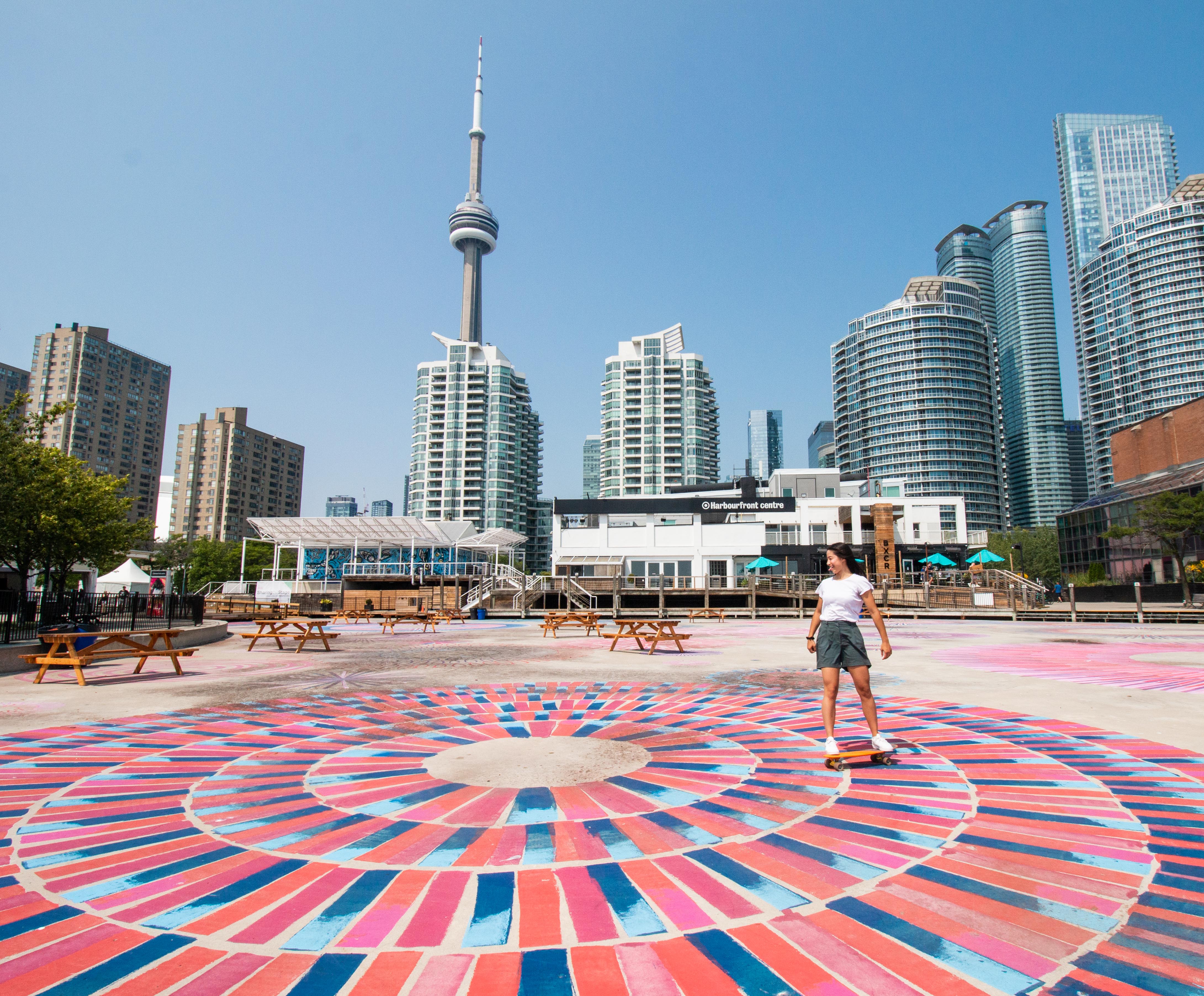 A teenager skates on colourful pavement with shops and skyscrapers in the background