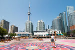 A teenager skates on colourful pavement with shops and skyscrapers in the background